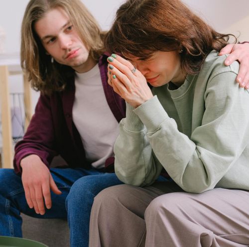 Crop male soothing disappointed crying female in sweatshirt and gray trousers on blurred background