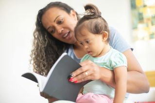 A mother and her young daughter enjoy reading a book together, fostering early learning.